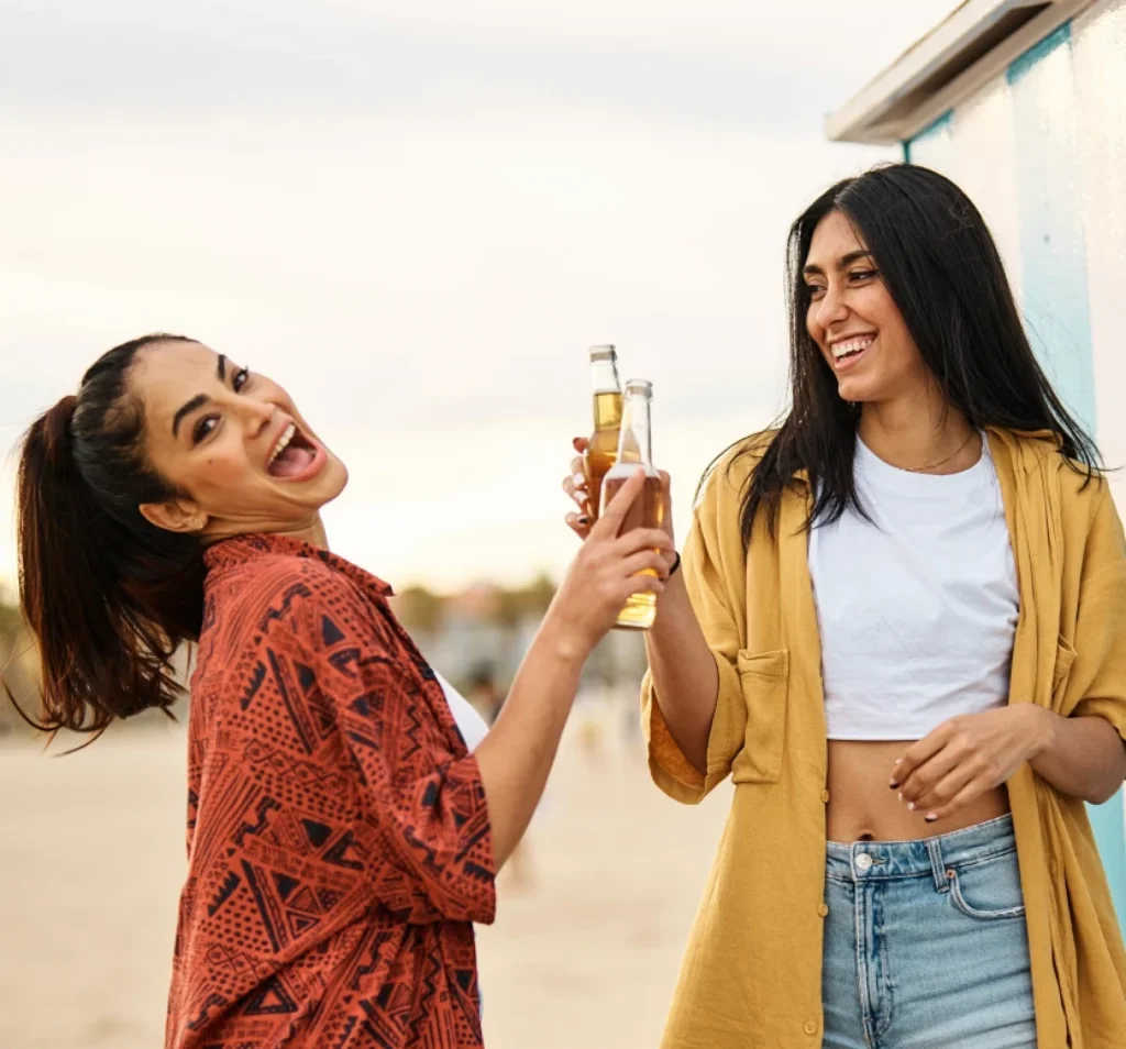 Two women smiling and enjoying drinks together outdoors on a sunny day